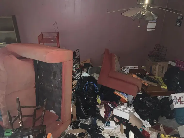 The inherited house as he found it &mdash; a living room filled floor to ceiling with furniture, bin bags and boxes, an overturned armchair against a mauve wall.
