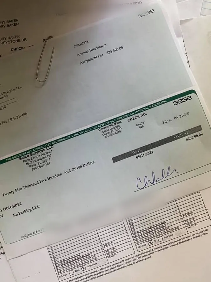 The closing paperwork on his desk: an amount breakdown dated 05/21/2021 showing an assignment fee of $25,500.00, the escrow cheque for the same amount beneath it, and the settlement statement underneath. Bank account numbers have been obscured.